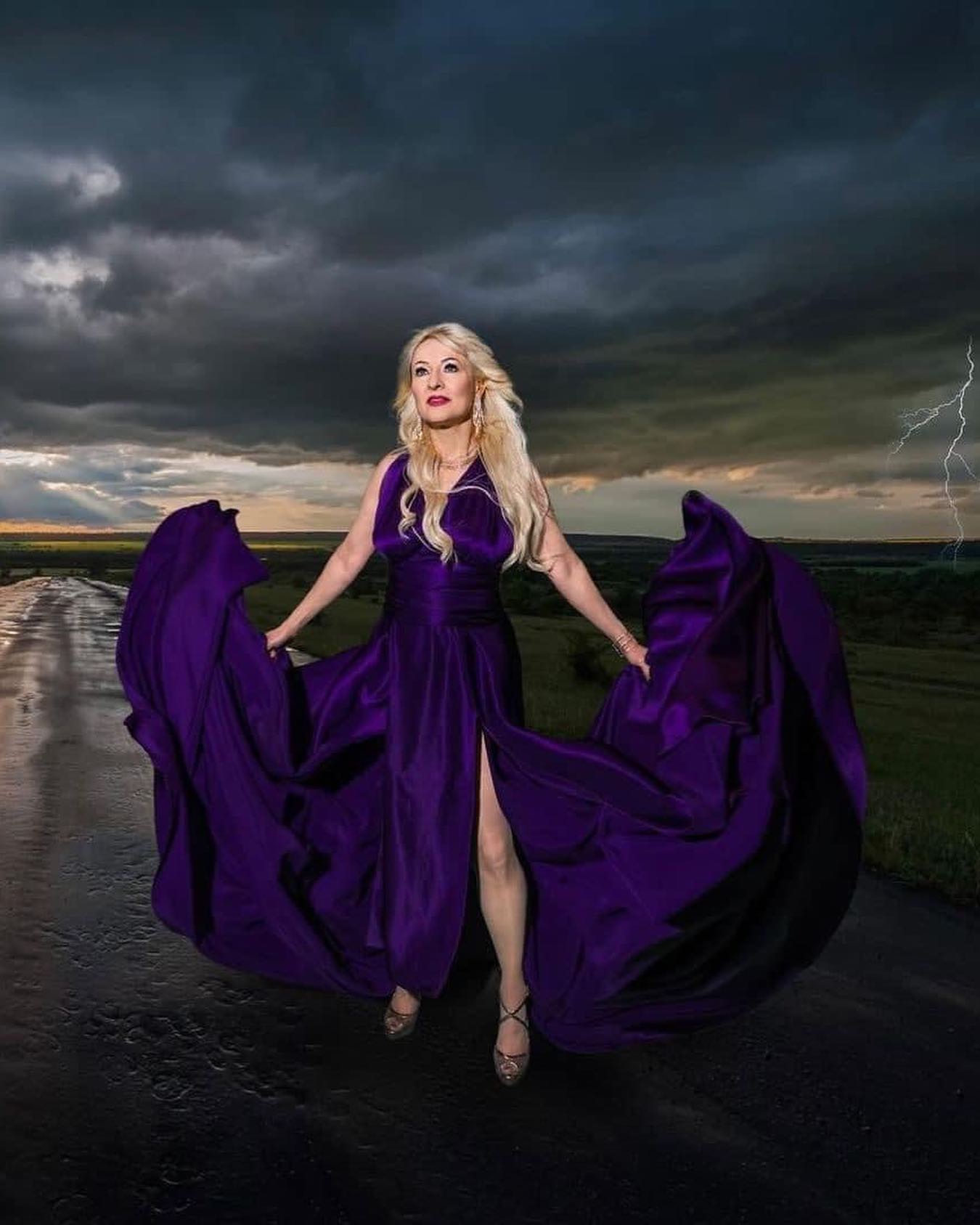 Hunter Storm standing on a wet road, channeling the storm as a sorceress in a vibrant royal purple Santorini dress.