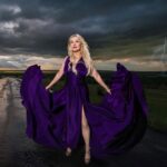 Hunter Storm standing on a wet road, channeling the storm as a sorceress in a vibrant royal purple Santorini dress.