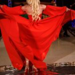 Hunter Storm, The Metal Valkyrie, strutting down the runway in red, showcasing a dynamic walk, swirling fabric, and metallic gold sequin Christian Louboutin red bottom stilettos.